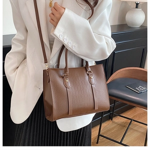 Detail of a brown crocodile leather tote bag featuring a textured finish and sturdy handles