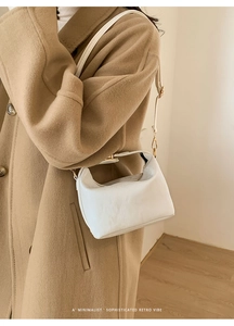 Close-up of a white minimalist handbag with lychee texture and metallic clasp handle