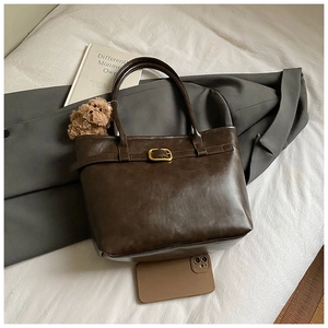 Detail of vintage brown tote bag with bear charm and golden buckle on white fabric