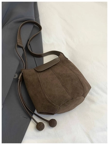 Vue détaillée du sac seau en daim marron avec cordon en cuir et pendentif boule