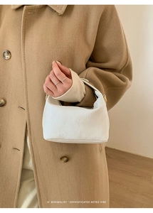 Close-up of minimalist white retro pillow bag with textured fabric and golden metal parts