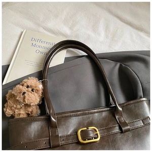 Detail of dark brown leather tote bag featuring golden buckle and top dog plush charm