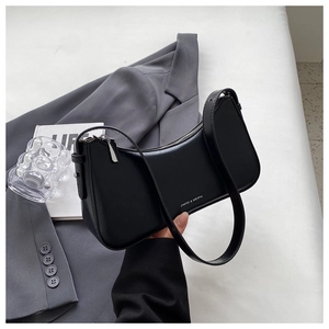 Detail of minimalist black faux leather crescent shoulder bag with metallic logo and zipper