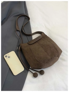 Détail du sac seau en daim marron avec cordon à perles et blazer gris élégant