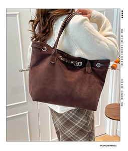 Detail of a large dark brown suede tote bag with silver buckle and decorative belt strap