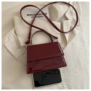 Détail du sac à main bordeaux en cuir verni avec téléphone illustrant sa petite taille