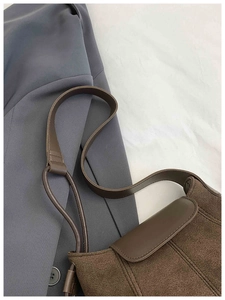 Detail of dark brown leather handbag with flap closure on a gray suit jacket background
