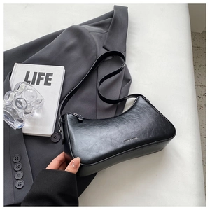 Close-up of black leather baguette bag with litchi texture and silver logo lettering