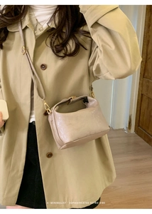 Close-up of beige textured mini crossbody bag with gold hardware worn by a model