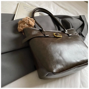 Close-up of brown textured leather tote bag with gold metal buckle and plush bear charm