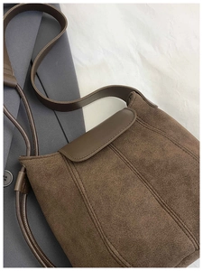 Close-up of vintage brown suede bucket bag with leather strap and vertical stitching detail