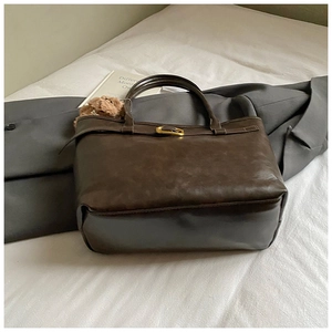 Detail of deep brown retro leather tote bag featuring a gold metal buckle on white fabric