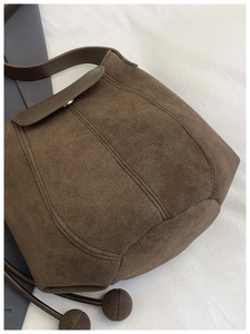 Detail of dark brown suede bucket bag featuring unique ball pendants and top flap