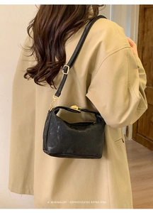 Close-up of black retro textured crossbody bag with gold buckle on trench coat model