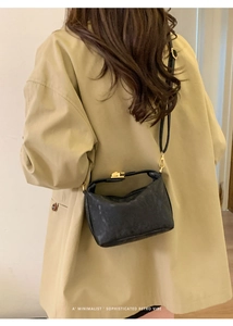Black leather hobo bag with gold metal buckle shown on a model in a beige trench coat