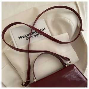 Gros plan du sac à main en cuir verni rouge foncé sur tissu blanc et vieux livres