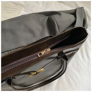 Detail shot of the golden metal zipper closure and reinforced stitching on dark brown tote bag
