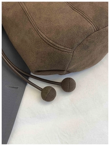Detailed view of dark brown suede bag featuring stitching craftsmanship and drawstring balls