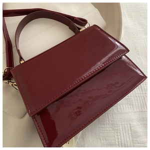 Détail macro du sac à main en cuir verni bordeaux avec boucles dorées et poignée ronde