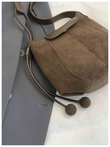 Detail of brown suede bucket bag featuring drawstring closure with unique ball ornaments