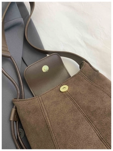 Detail of dark brown suede shoulder bag with magnetic clasp and decorative stitching