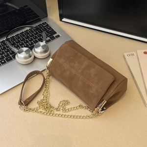 Brown suede and leather tote bag with quilted stitching and gold chain strap on desk