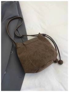 Detail der dunkelbraunen Wildleder-Beuteltasche mit Kordelzug und weichen Pompon-Akzenten