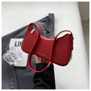 Detail of red crescent shoulder bag featuring silver metal logo on shiny leather finish