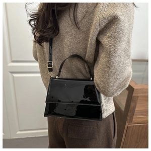 Sac bandoulière trapèze en cuir verni noir brillant avec détails dorés porté par mannequin