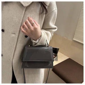 Détail d'un sac à main gris en cuir verni montrant sa forme trapèze et sa poignée chic
