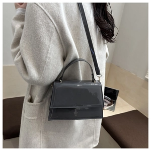 Sac à main en cuir verni gris foncé porté sur un manteau en laine beige élégant