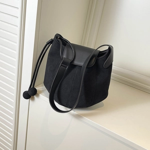 Minimalist black matte suede bucket bag with round drawstring detail on a white surface