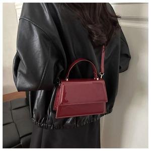 Détail d'un sac en cuir verni bordeaux avec garniture dorée porté sur un blouson en cuir