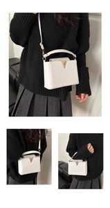 Detailed close-up of white leather handbag with gold V-buckle and textured finish