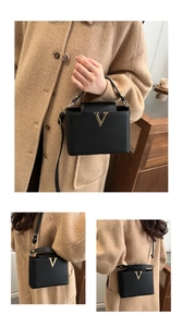 Detailed view of black textured leather bucket bag with gold V-shaped metal hardware