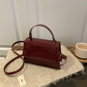 Sac à main trapèze en cuir verni rouge foncé avec détails dorés et bandoulière