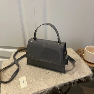 Sac à main minimaliste en cuir verni gris foncé avec poignée sur une surface en peluche