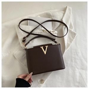 Detailed macro view of dark brown pebbled leather bag with gold V-shaped metal hardware