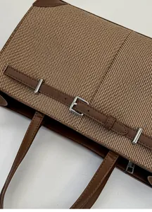 Detail of brown twill tote bag with dark leather straps and silver buckle closure