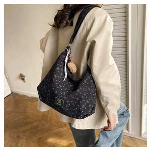 Détail du sac à bandoulière en toile noire avec motif nœud blanc et breloque peluche