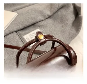 Detailed close-up of dark brown oil wax leather bag handle with golden metal buckles