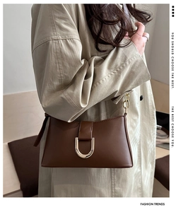 Détail d'un sac bandoulière en cuir marron avec boucle dorée en U et bandoulière chaîne