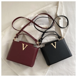 Close-up of burgundy and black pebbled leather bags with gold V-logo on white fabric