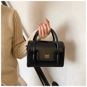 Detail of black patent leather handbag featuring gold metal logo and sleek top handle