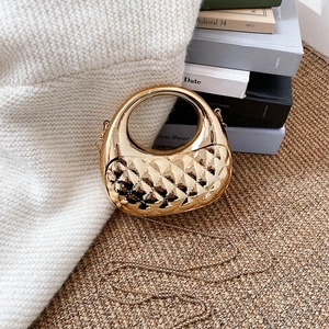 Mini gold acrylic handbag with quilted pattern and large ring handle on a cozy knit blanket