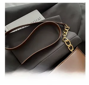 Détail du sac en cuir marron avec chaîne dorée et boucle sur un costume gris