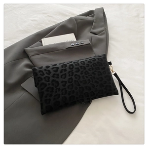 Detail of black leopard print clutch bag featuring gold hardware and a wristlet strap
