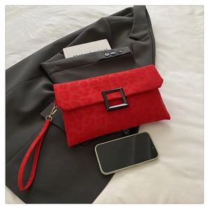 Detail of red leopard texture clutch with black square buckle and wrist strap on a bed