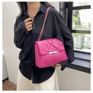 Close-up of rose red quilted crossbody bag with metal chain strap worn by a model