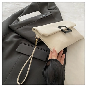 Detailed texture of cream envelope clutch bag featuring a minimalist matte black square buckle